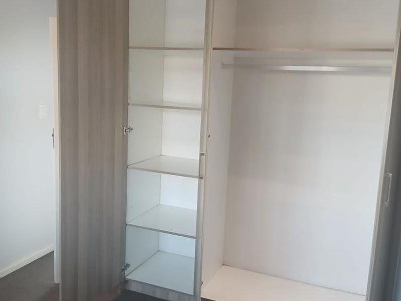 A bedroom featuring a modern, light-wood finish built-in wardrobe with integrated shelving and a hanging rail.