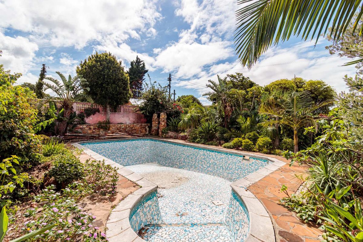 An outdoor pool area featuring a tiled swimming pool, stone paving, and established garden surroundings, currently requiring maintenance and refurbishment.