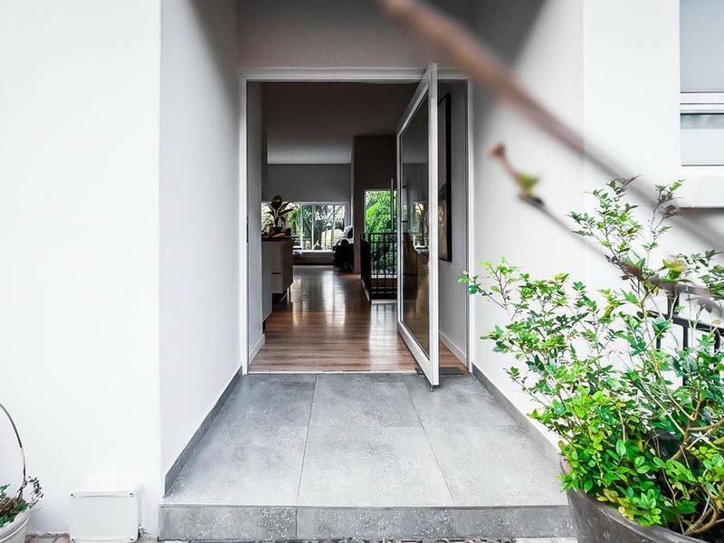 Inviting entrance featuring a modern glass pivot door, tiled porch area, and a view into the open-plan living space with hardwood flooring.
