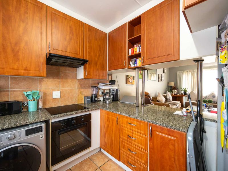 A functional kitchen featuring warm-toned wooden cabinetry, granite countertops, a built-in oven and hob, and a convenient breakfast bar overlooking the living area.