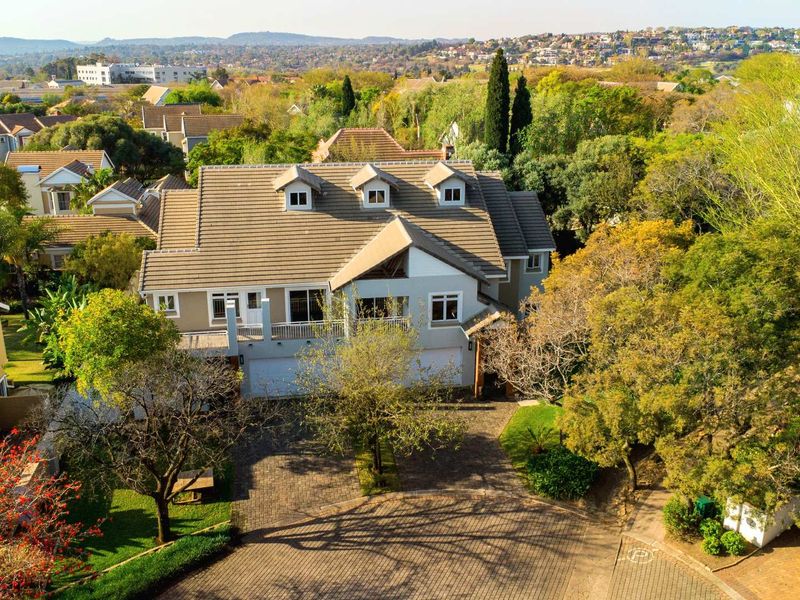 Aerial view of a multi-story residential property featuring a tiled roof, double garage, and paved driveway set within a landscaped suburban environment.