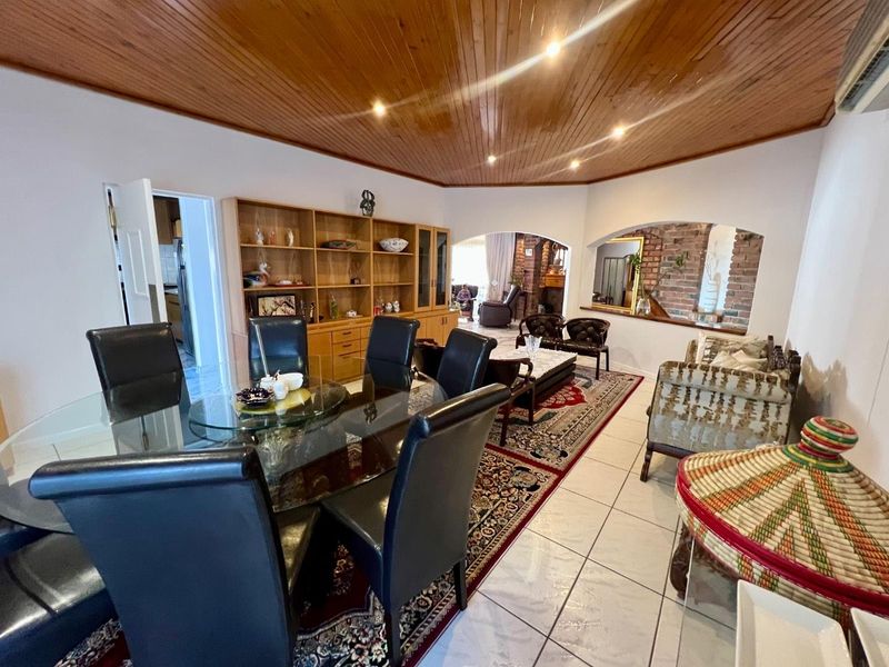 Spacious open-plan living and dining area featuring a distinctive timber ceiling, ceramic tiled flooring, and an exposed brick archway connecting to adjacent spaces.