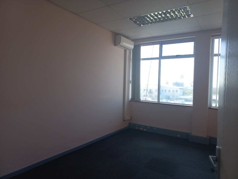 A vacant office space featuring a suspended ceiling, recessed lighting, split-system air conditioning, and large windows providing natural light.