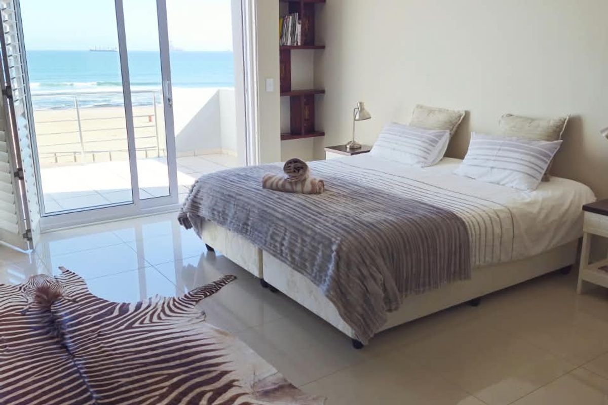 Spacious bedroom featuring tiled flooring, built-in shelving, and large sliding glass doors opening onto a balcony with direct ocean views.