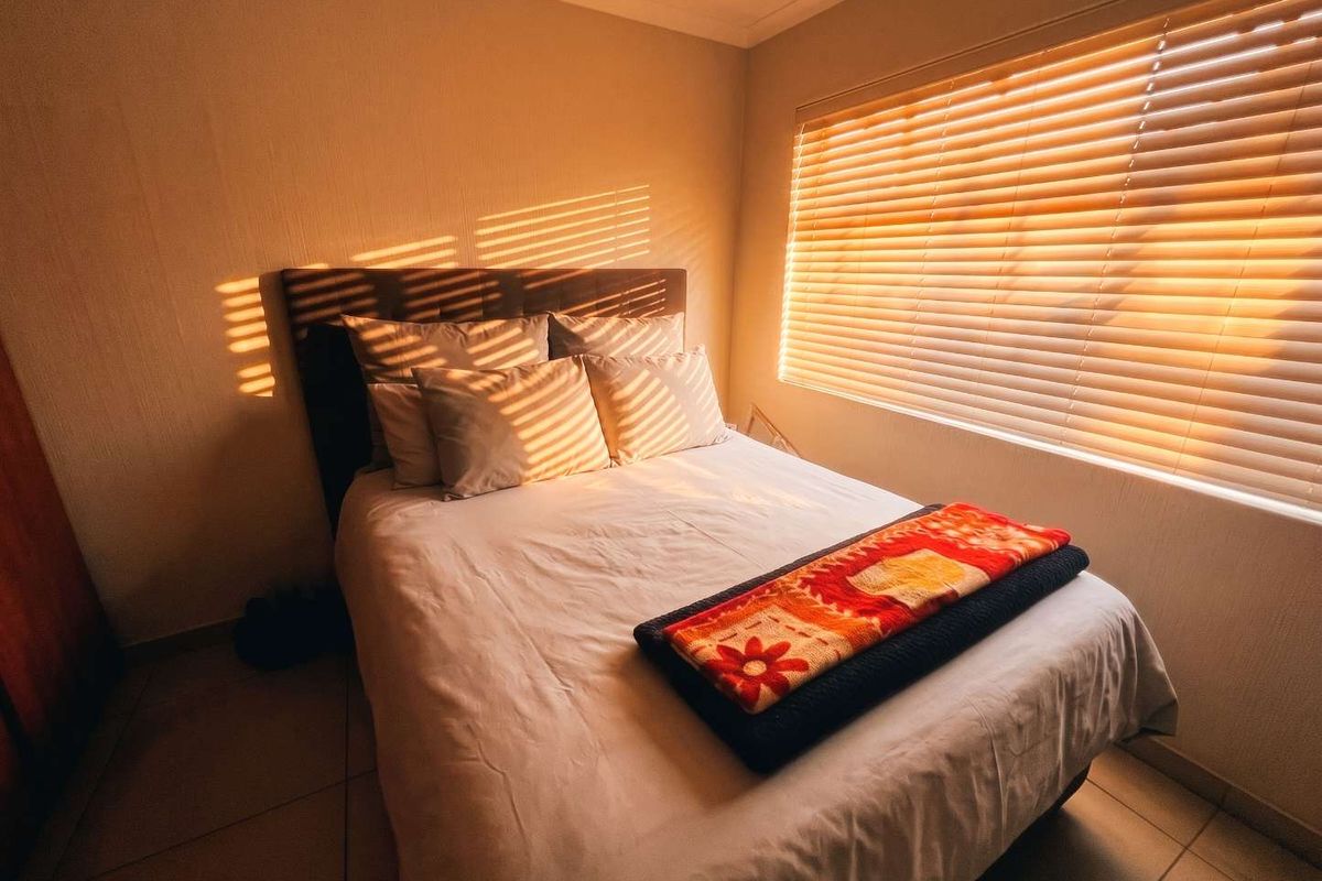 A cozy bedroom featuring tiled flooring, coved ceilings, and venetian blinds that allow for warm, natural light.