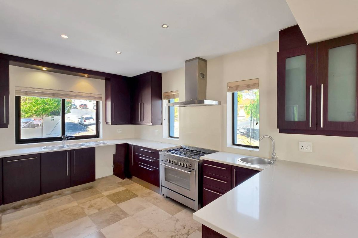 Modern kitchen featuring dark wood cabinetry, stone countertops, stainless steel gas stove with extractor fan, and tiled flooring.