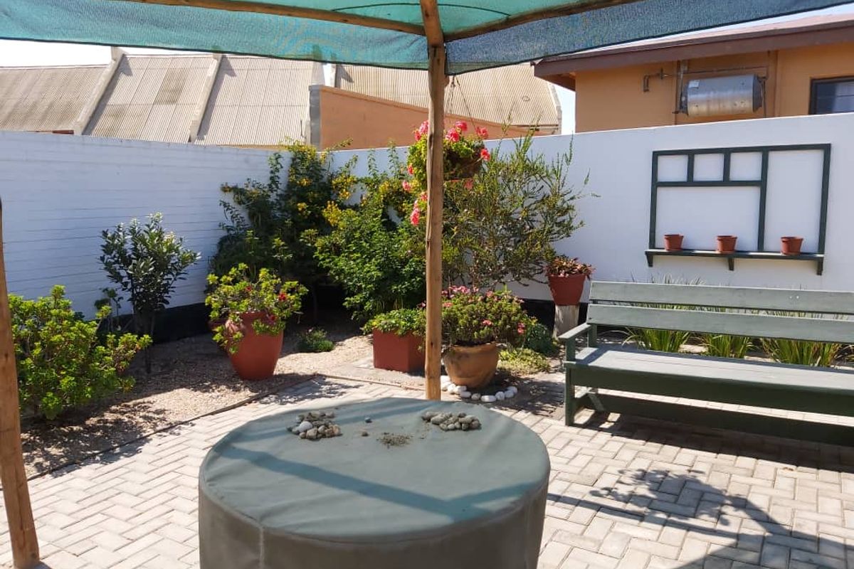 A private rear courtyard featuring paved flooring, a shaded seating area, perimeter boundary walls, and established garden beds.
