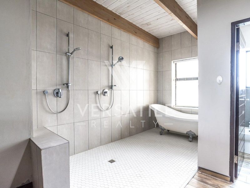 Spacious bathroom featuring a dual shower setup, a classic freestanding clawfoot bathtub, and exposed timber ceiling beams with modern neutral tiling.