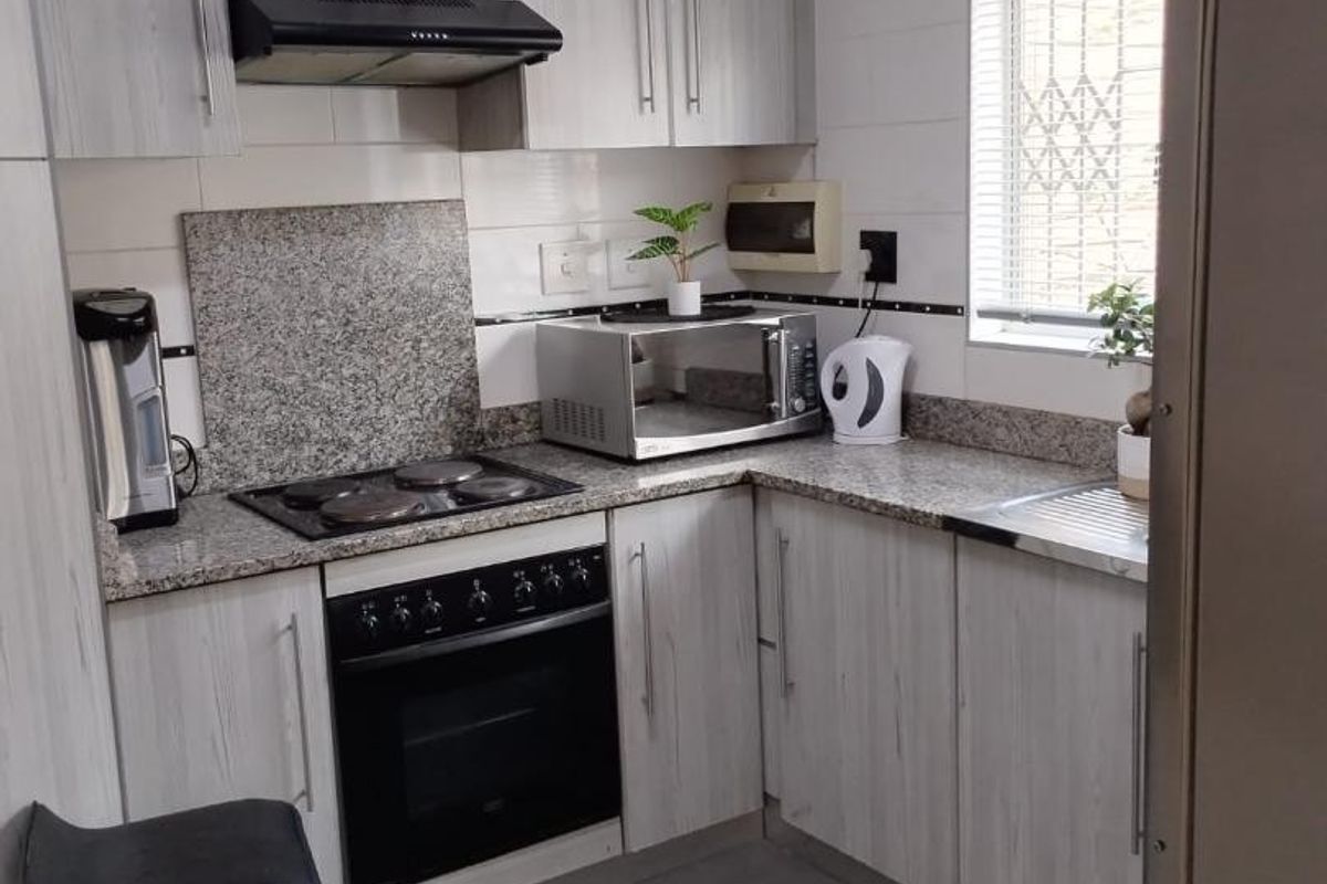 Compact kitchen featuring light wood-grain cabinetry, granite countertops, built-in oven, electric hob, and a tiled backsplash.
