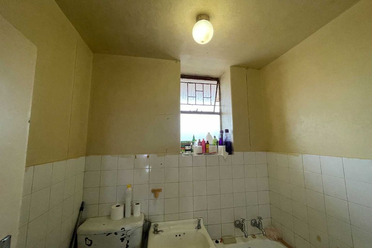 A dated bathroom featuring a standard bathtub, basin, and toilet, requiring significant renovation and cosmetic updates to improve its condition and functionality.