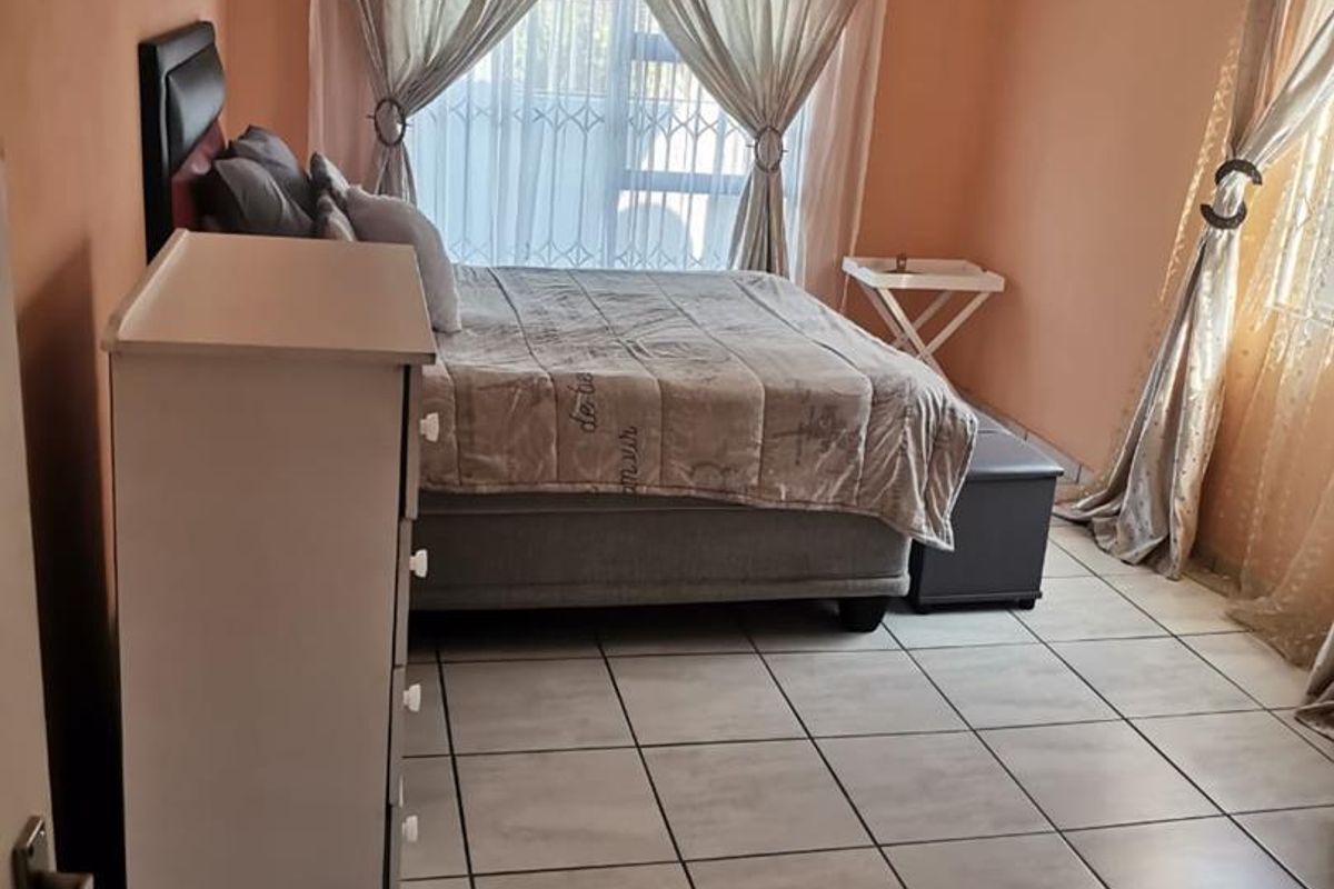 A bedroom featuring tiled flooring, large windows with security bars, and neutral wall finishes.