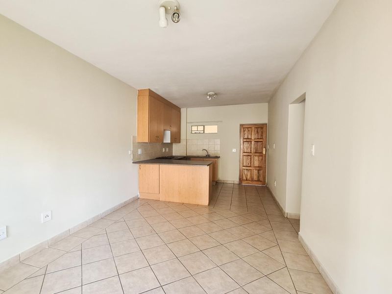 Open plan living and kitchen area featuring tiled flooring, built-in wooden cabinetry, and a solid timber entrance door.