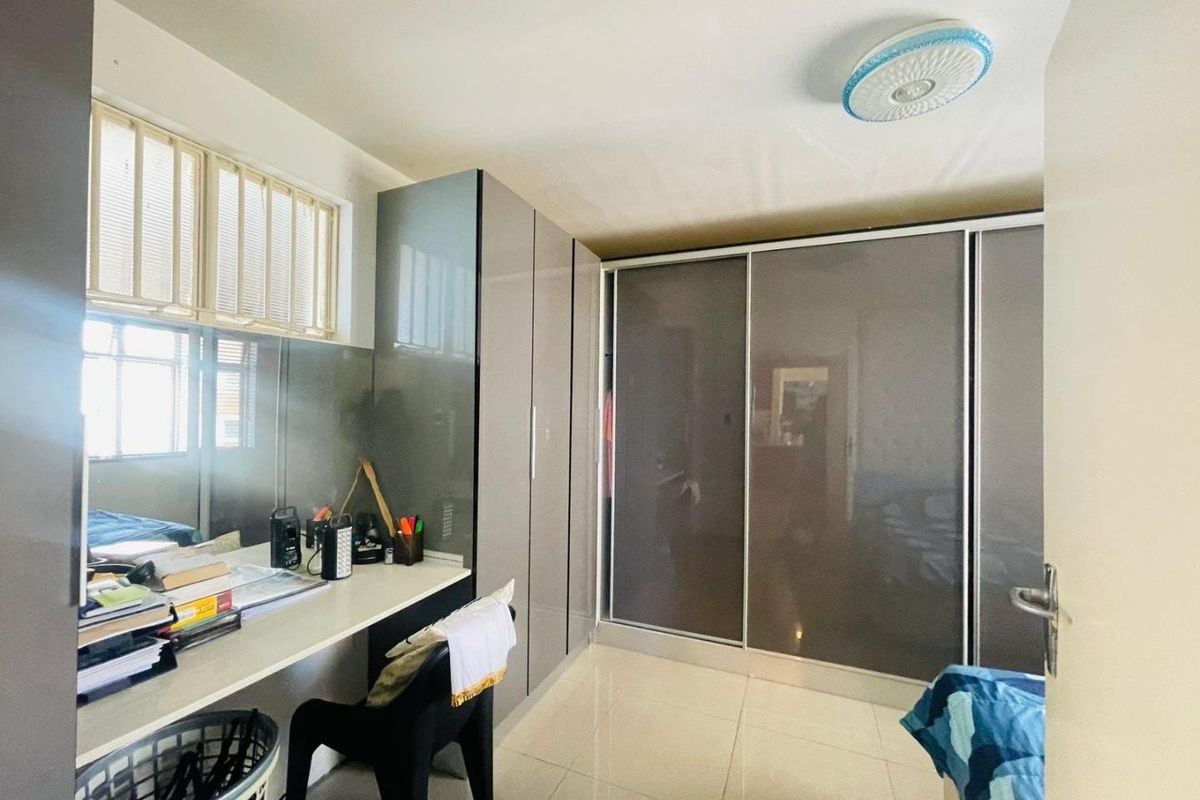 A bedroom featuring built-in cupboards with sliding doors and an integrated desk area, finished with tiled flooring.
