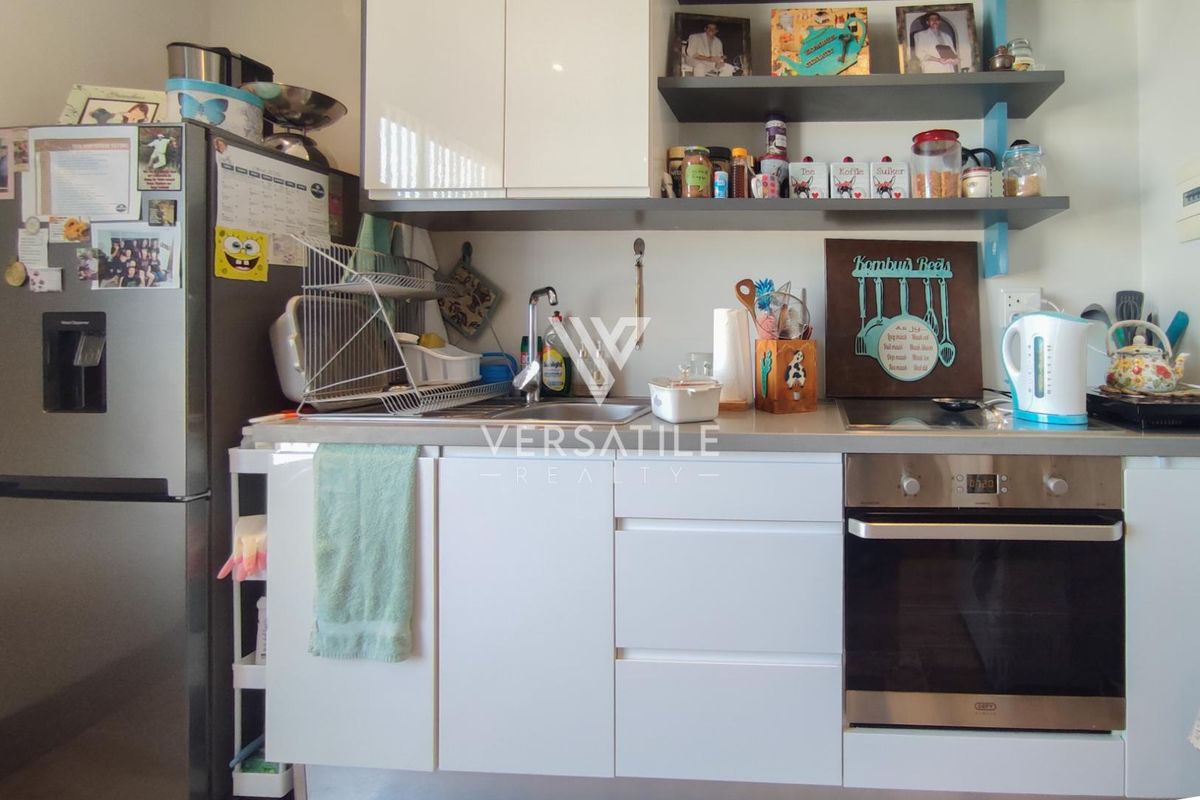 Compact kitchen featuring modern white cabinetry, stainless steel sink, built-in oven, and open shelving for storage.