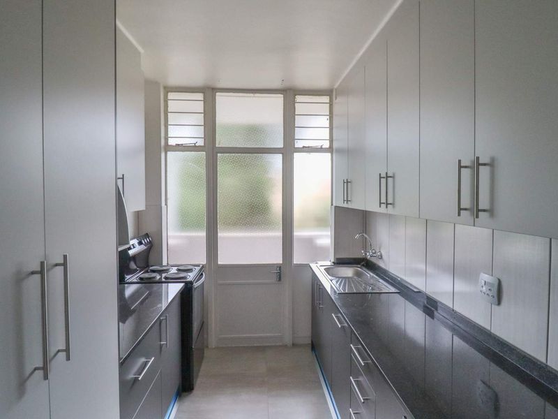 A clean, galley-style kitchen featuring modern dark stone countertops, ample white cabinetry, and a functional electric stove with direct access to an exterior door.