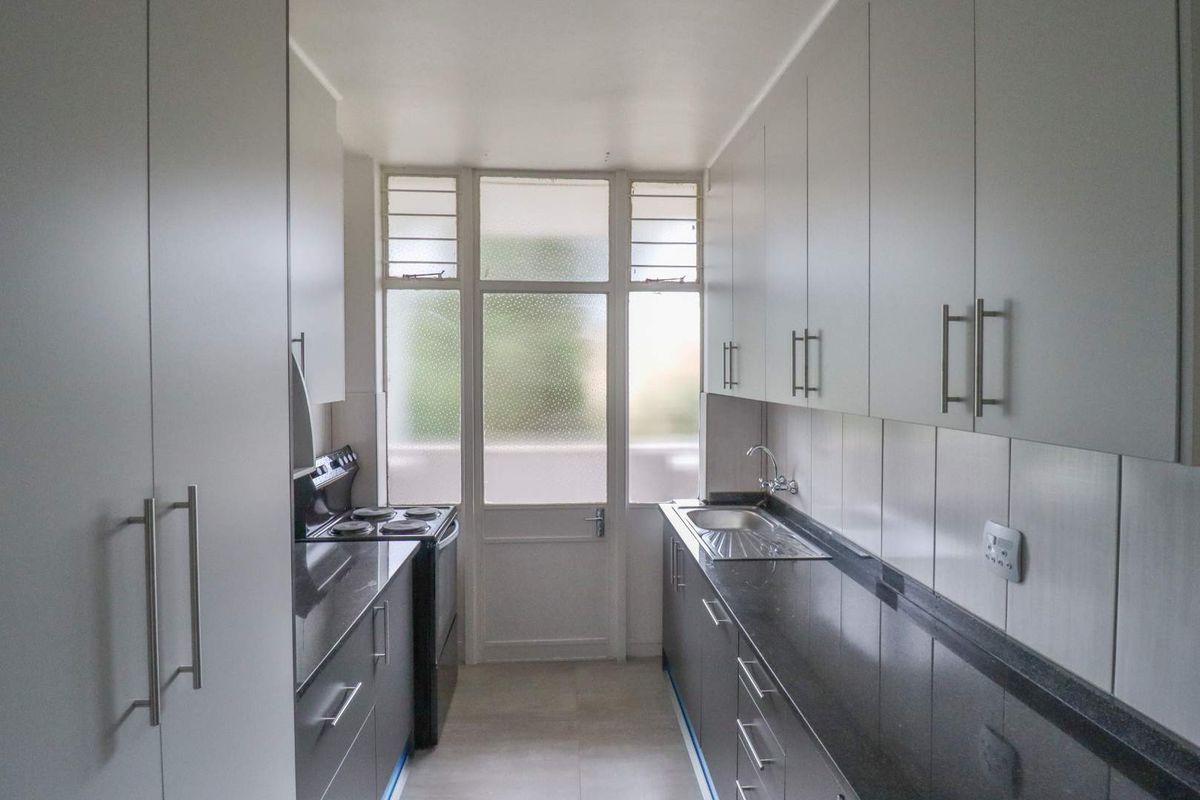 A clean, galley-style kitchen featuring modern dark stone countertops, ample white cabinetry, and a functional electric stove with direct access to an exterior door.