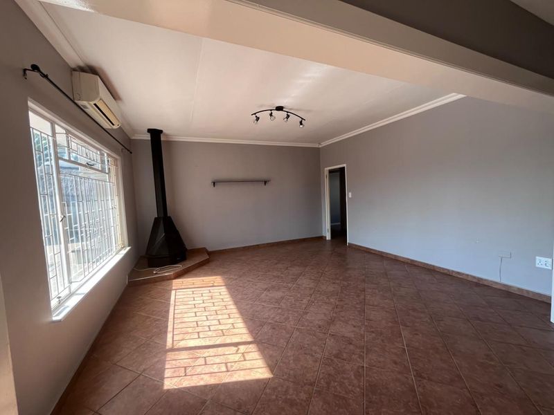 Spacious living area featuring tiled flooring, a freestanding fireplace, and a wall-mounted air conditioning unit.