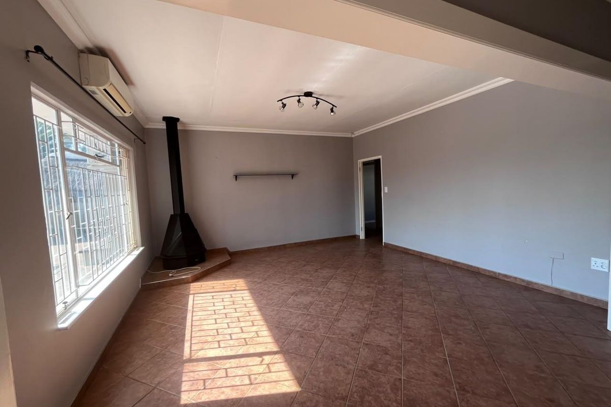 Spacious living area featuring tiled flooring, a freestanding fireplace, and a wall-mounted air conditioning unit.