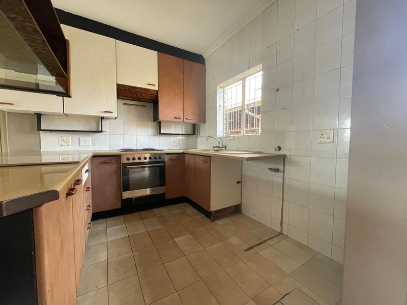 A dated kitchen featuring built-in cabinetry, an integrated oven and hob, tiled splashbacks, and tiled flooring, requiring cosmetic updates and repairs.