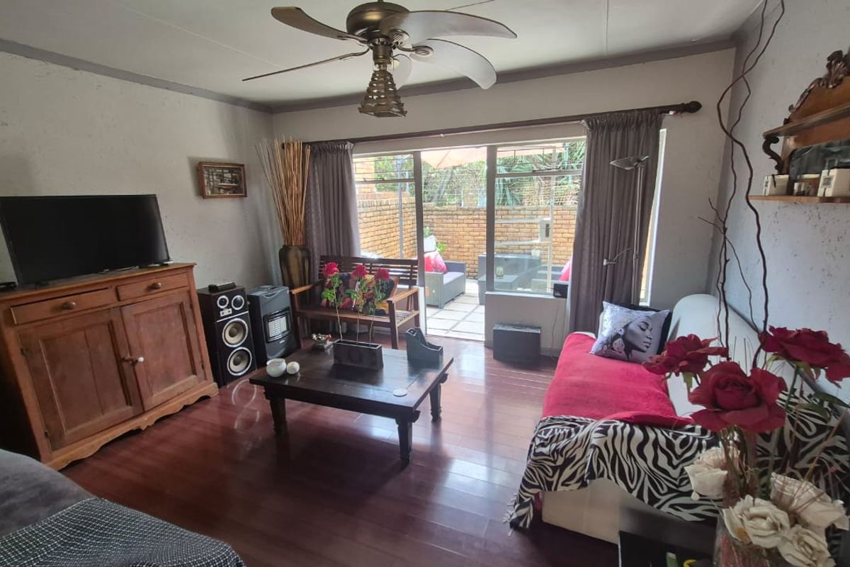 A living room featuring laminate flooring, a ceiling fan, and a sliding glass door providing access to an outdoor patio area.