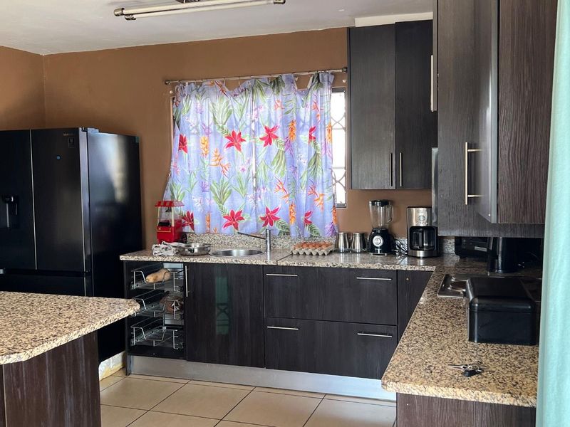 A functional kitchen featuring dark wood-grain cabinetry, granite countertops, a stainless steel sink, and tiled flooring.