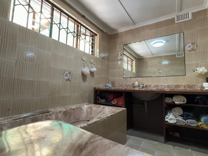 A dated bathroom featuring a built-in bathtub, vanity with integrated basin, and full-height wall tiling, requiring modernization to improve aesthetic appeal.