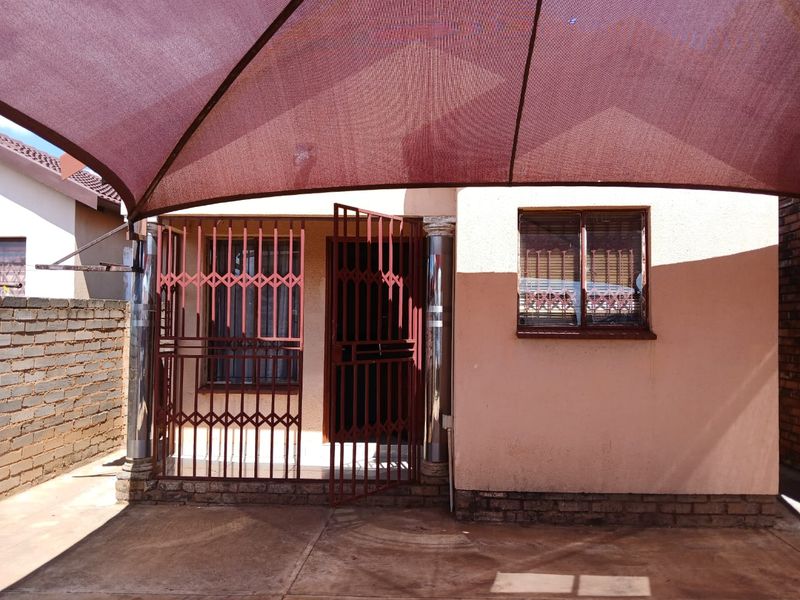 Covered patio area featuring a shade sail, security gates, and concrete paving, providing a functional outdoor space for relaxation or entertainment.