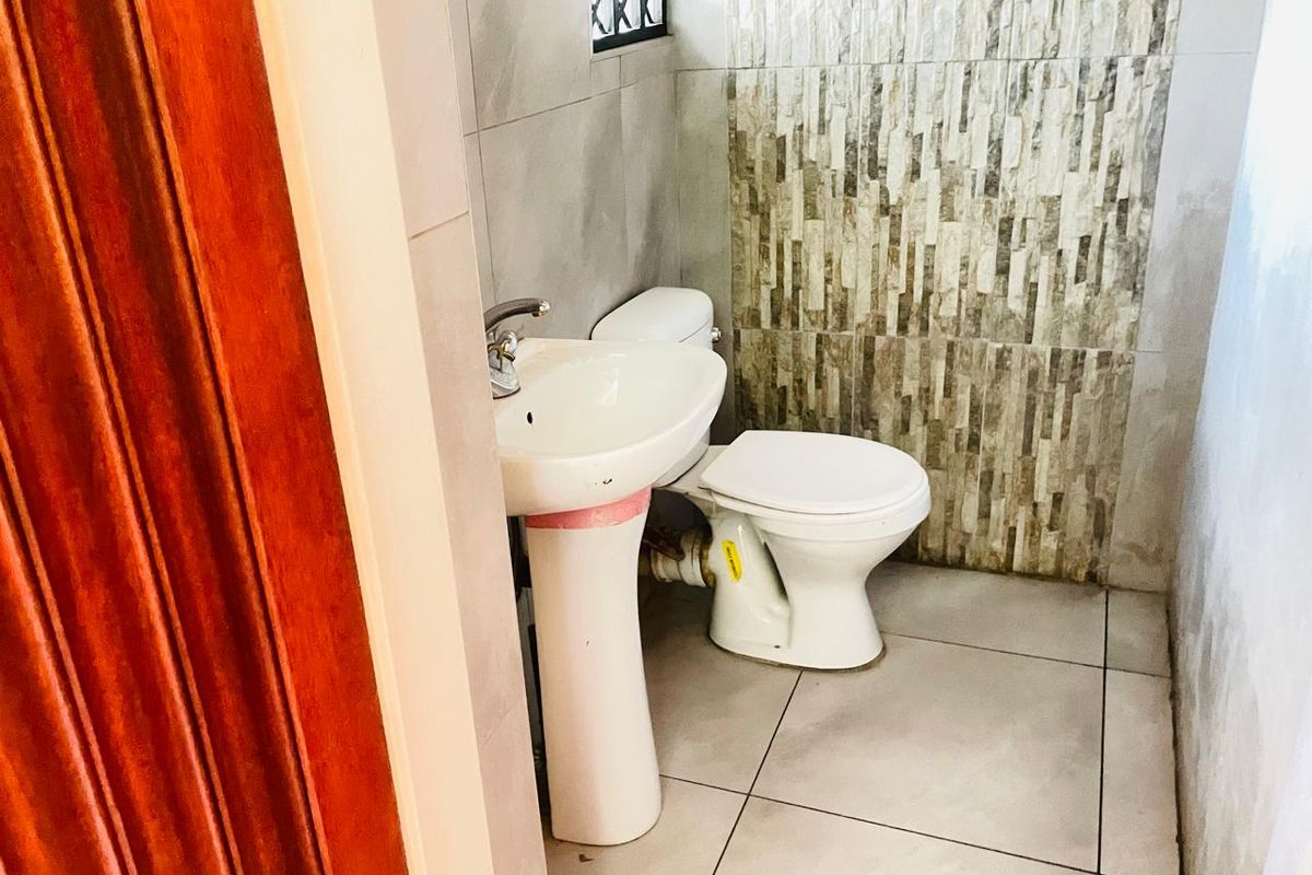 A compact bathroom featuring a pedestal sink, a standard toilet, and decorative stone-effect wall tiling.