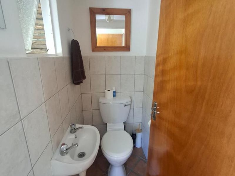 A compact guest bathroom featuring a wall-mounted basin, toilet, tiled walls, and terracotta-style floor tiles.