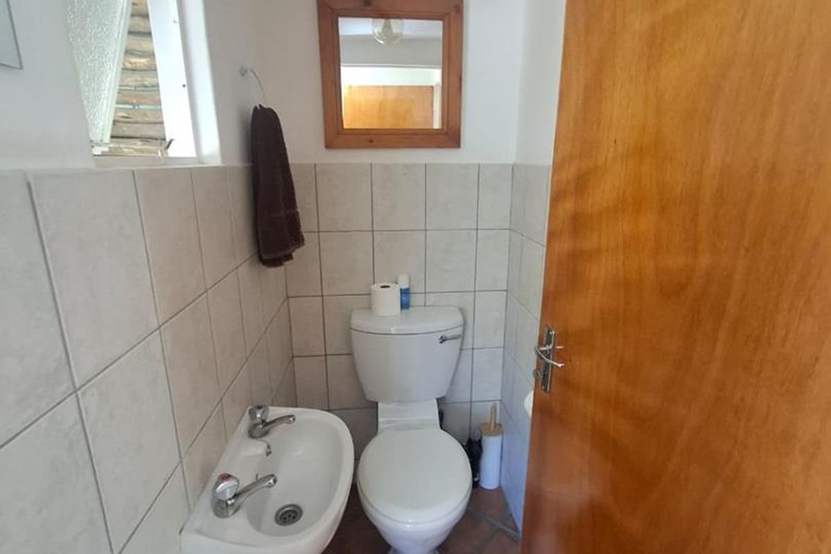A compact guest bathroom featuring a wall-mounted basin, toilet, tiled walls, and terracotta-style floor tiles.
