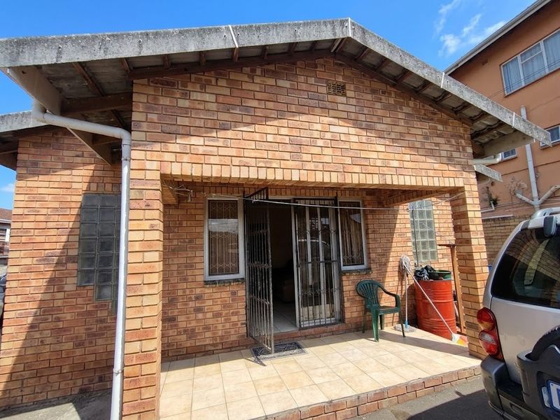 Front elevation of a face brick cottage featuring a covered tiled patio, security gate, and glass block window accents.