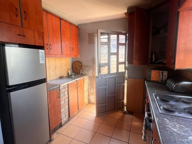A functional kitchen featuring built-in cabinetry, tiled flooring, and a stable door leading to the exterior. The space would benefit from modern updates.