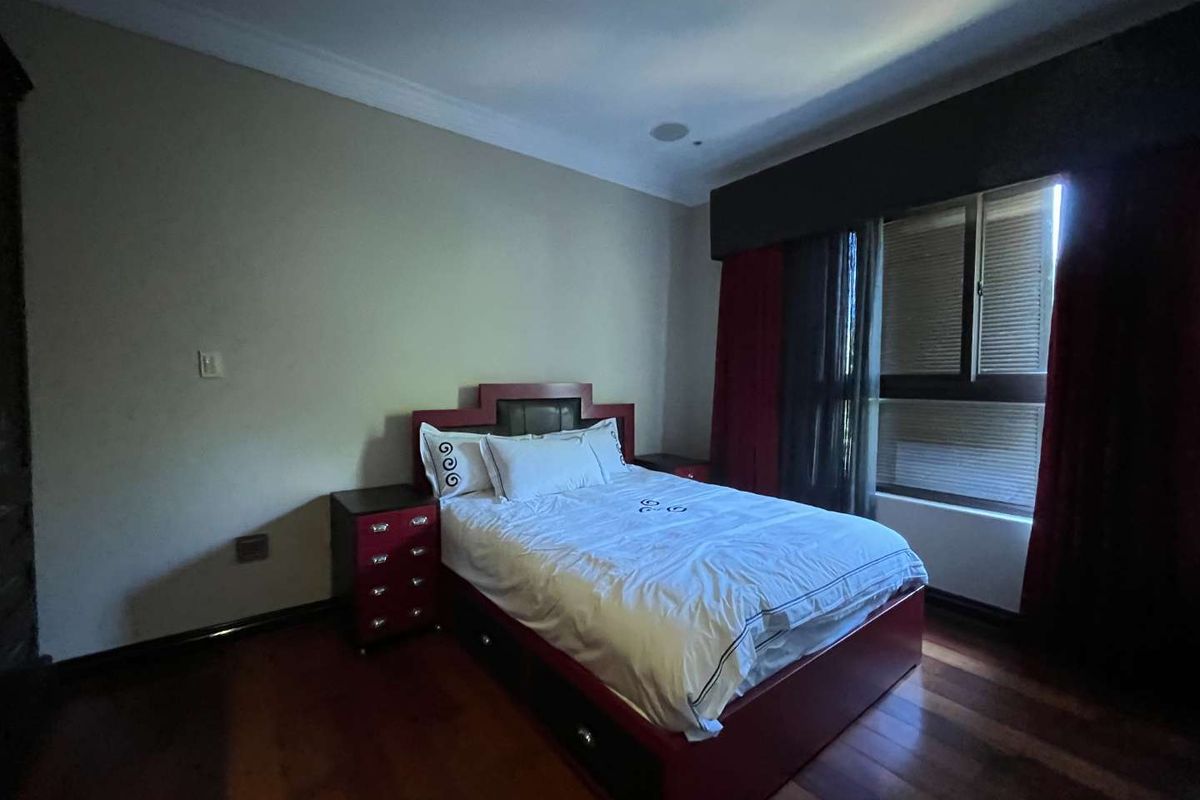 A bedroom featuring polished timber flooring, recessed ceiling lighting, and a large window with integrated blinds.