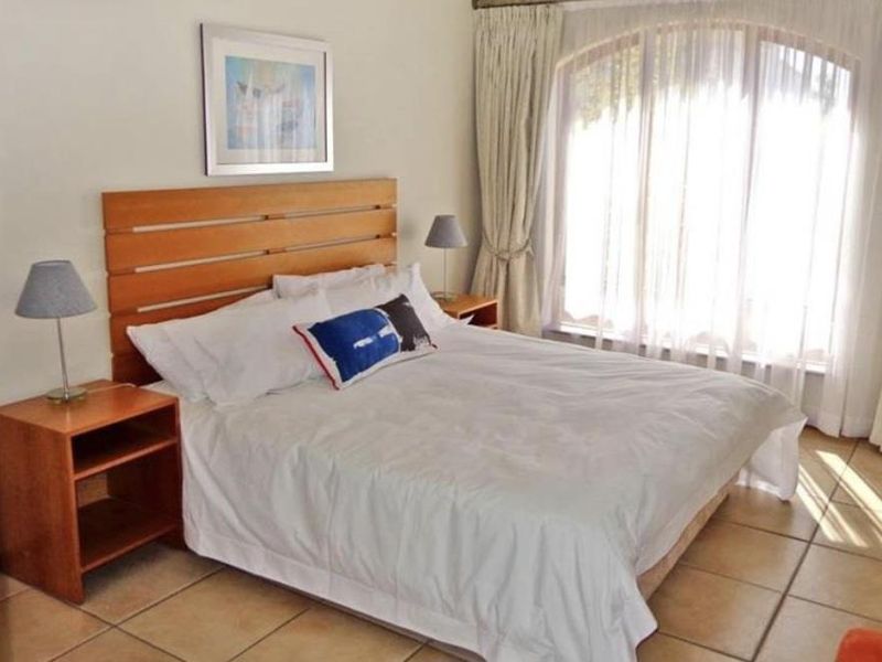 A well-lit bedroom featuring tiled flooring and a large arched window with curtains, providing a comfortable and functional living space.