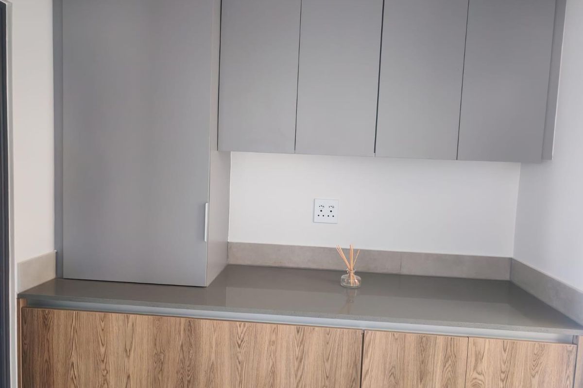 A modern kitchen area featuring sleek grey upper cabinetry, wood-grain lower cabinets, and a durable stone countertop with a tiled backsplash.