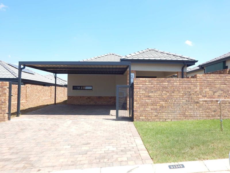 Front view of a modern house featuring a paved driveway, a covered carport, and a brick boundary wall with a neat lawn.