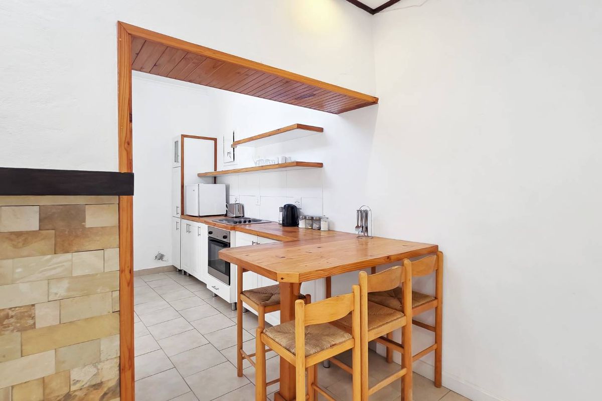 Compact kitchen featuring white cabinetry, timber shelving, a built-in oven and hob, and an integrated timber breakfast bar area.