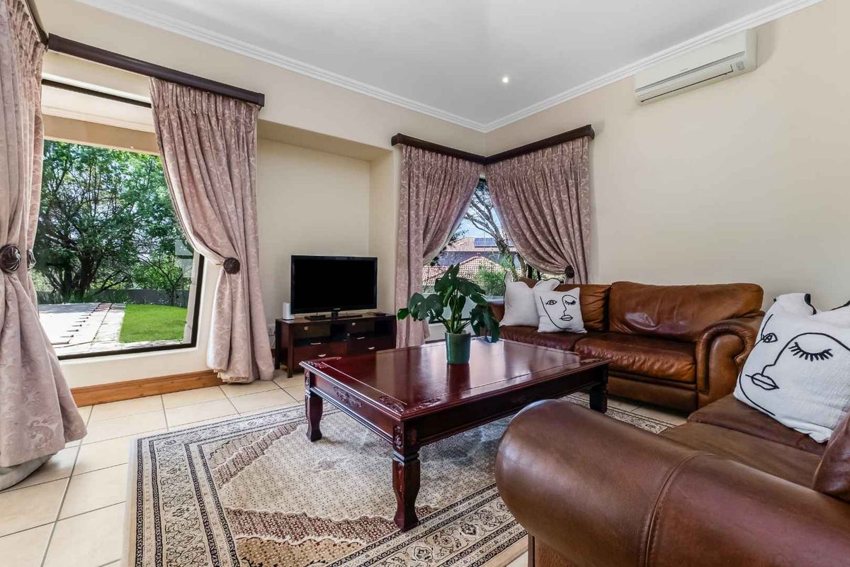 A comfortable living room featuring tiled flooring, recessed lighting, and large windows with garden views, equipped with a wall-mounted air conditioning unit.