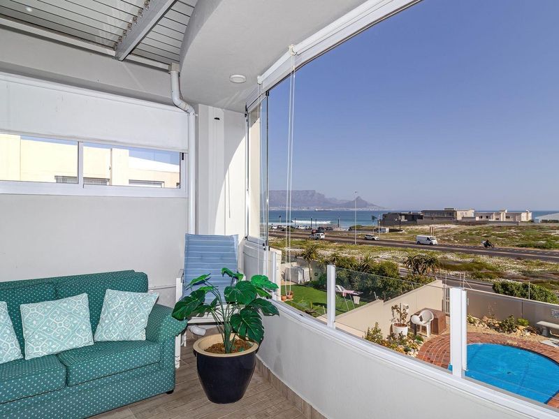 Covered balcony featuring a glass balustrade and retractable glass enclosure, offering expansive coastal and mountain views.