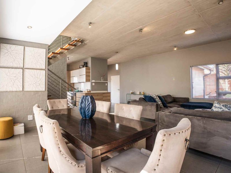 Spacious open-plan living and dining area featuring an exposed concrete ceiling, modern tiled floors, and a staircase with a contemporary metal railing.