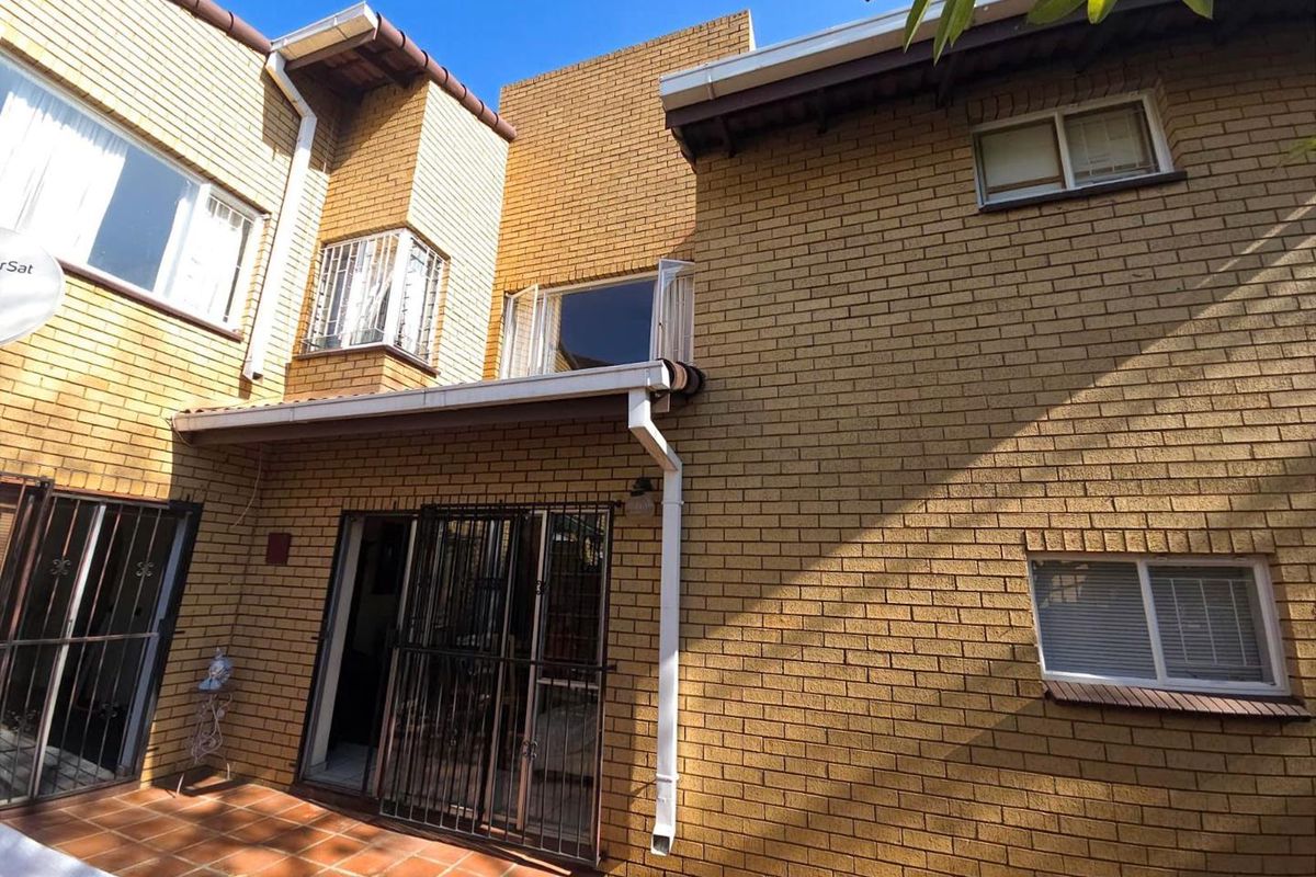 Rear view of the townhouse featuring face-brick exterior, tiled patio area, and security gates on sliding doors and windows.