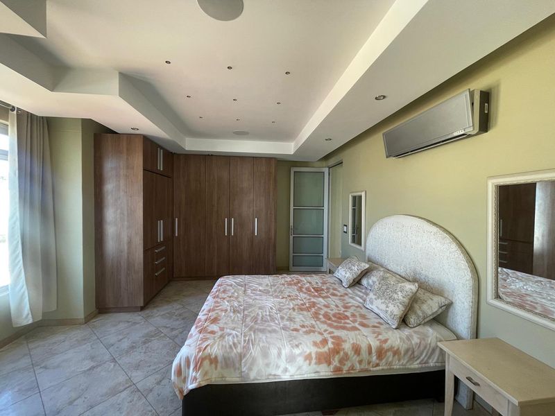 Spacious bedroom featuring built-in wooden cupboards, tiled flooring, a dropped ceiling with recessed lighting, and a wall-mounted air conditioning unit.