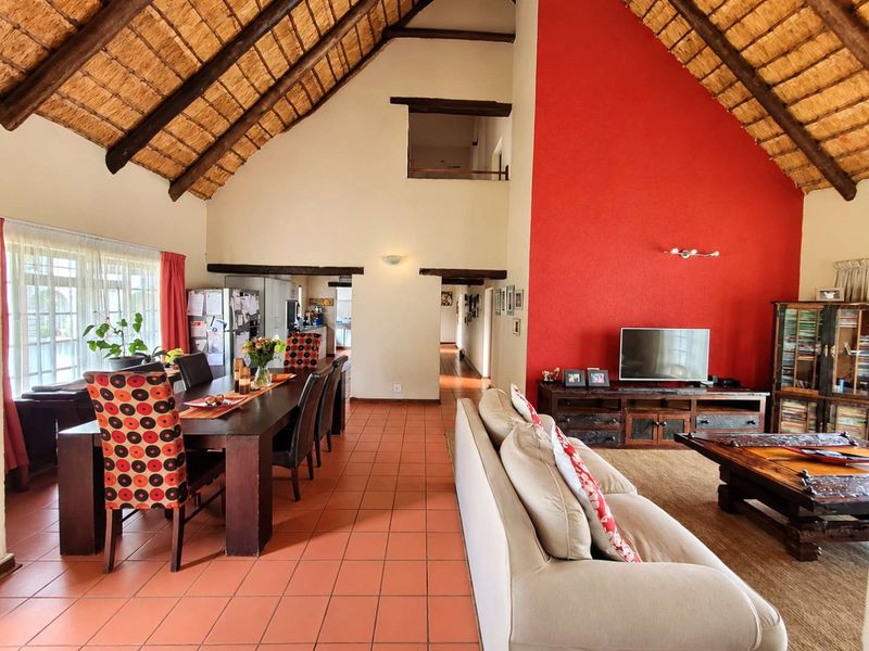Spacious open-plan living and dining area featuring a high vaulted thatched ceiling with exposed timber beams and distinctive terracotta floor tiles.