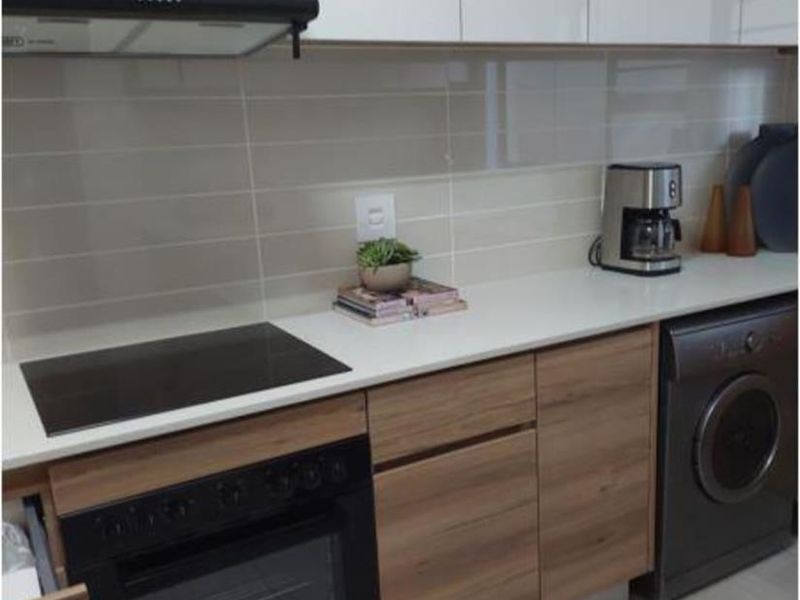 Modern kitchen featuring sleek two-tone cabinetry, stone countertops, built-in oven, electric hob, extractor fan, and integrated laundry appliance.