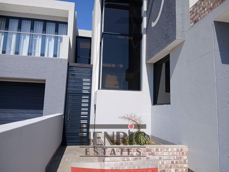 Modern double-storey apartment entrance featuring a striking glass facade, metal security gate, and paved driveway access.