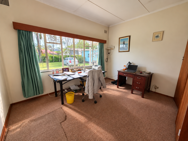 A functional home office space featuring a large window with garden views, built-in storage, and carpeted flooring.