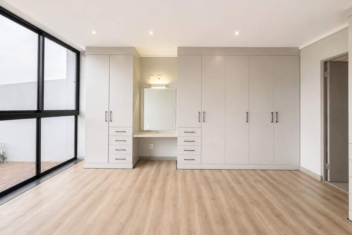 Spacious bedroom featuring extensive built-in cabinetry, a dedicated vanity area, modern laminate flooring, and large windows providing ample natural light.