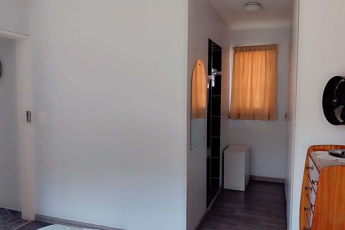 A bedroom interior featuring laminate flooring, a built-in cupboard, and a window with a curtain rail.
