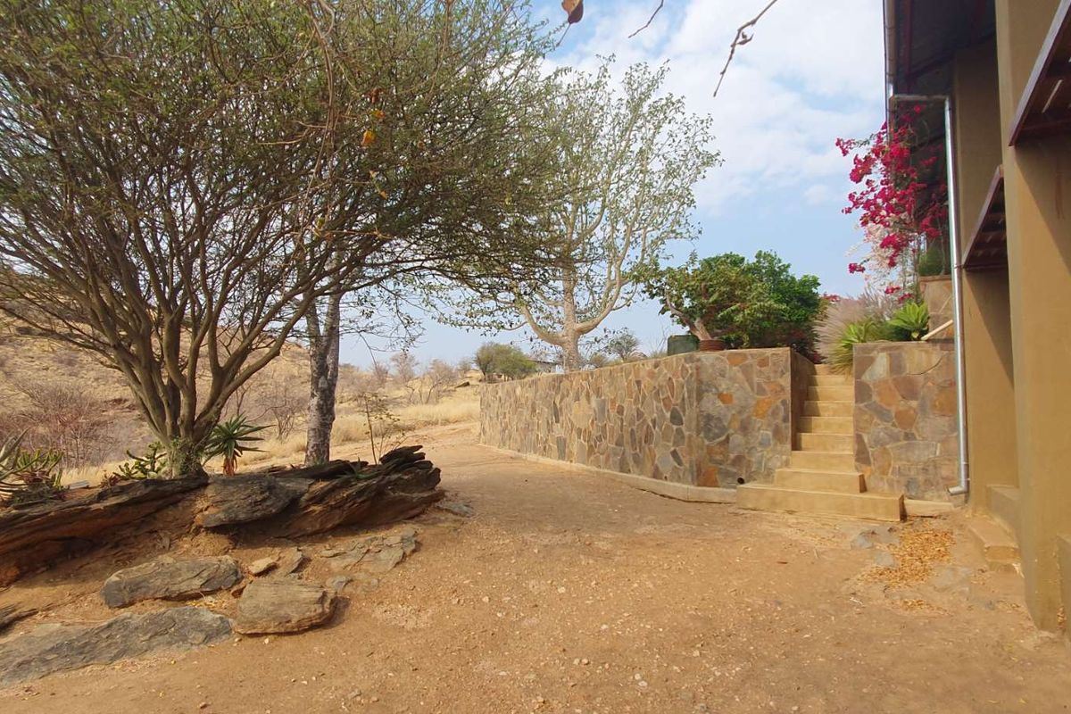 Outdoor area featuring a stone retaining wall, concrete steps, and natural landscaping with mature trees and rocky terrain.