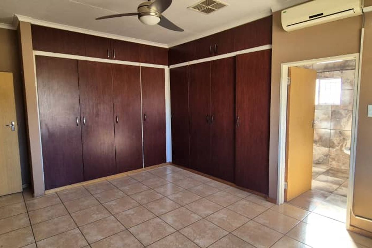 A bedroom featuring extensive built-in wooden cabinetry, tiled flooring, a ceiling fan, and an en-suite bathroom entrance.